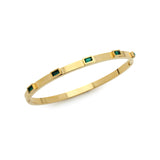 The Emerald Skinny Bangle, a sleek gold bracelet featuring six evenly spaced emerald-cut green gemstones set around its circumference. This minimalistic yet elegant bangle adds a refined touch of color and sophistication, perfect for stacking or wearing alone as a subtle statement piece.