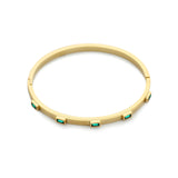 The Emerald Skinny Bangle, a sleek gold bracelet featuring six evenly spaced emerald-cut green gemstones set around its circumference. This minimalistic yet elegant bangle adds a refined touch of color and sophistication, perfect for stacking or wearing alone as a subtle statement piece.