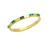 The Emerald Bangle, a gold bangle bracelet adorned with rectangular emerald green gemstones around.