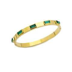 The Emerald Bangle, a gold bangle bracelet adorned with rectangular emerald green gemstones around.