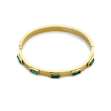 The Emerald Bangle, a gold bangle bracelet adorned with rectangular emerald green gemstones around.