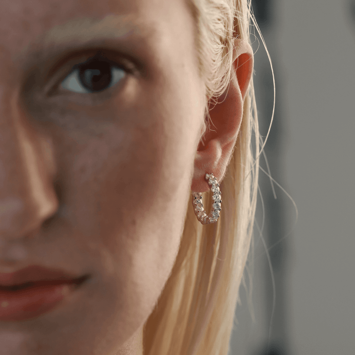 Model wearing the Wraparound Maxi Huggies, a pair of silver hoop earrings completely encrusted with sparkling cubic zirconia stones.