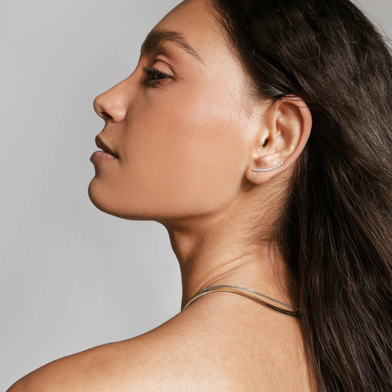 Model wearing one of the ear set which is a long arch earring filled with  surrounded with encrusted zirconia.