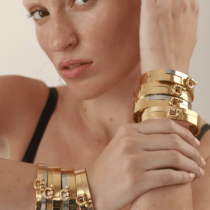 Model wearing stack of Herradura Bangles in gold and mix metals features a wide band with a contrasting gold and silver finish and a prominent, horseshoe-shaped clasp.||| GOLD