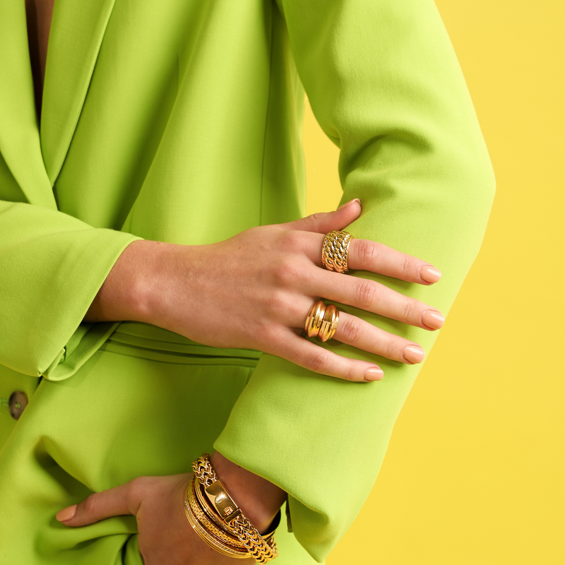 Model in green suit wearing the SPUNKY RING which is made of 18k gold plated brass which comes in two stackable rings and the braided ring. She is also wearing 4 gold bracelets.