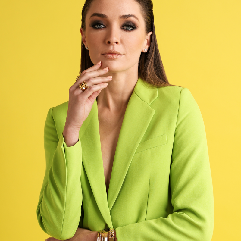 Model in green suit wearing the SPUNKY RING which is made of 18k gold plated brass which comes in two stackable rings and the braided ring. She is also wearing 4 gold bracelets.