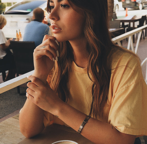 Model sitting in a restaurant wearing the Marinero bangle in gold with silver details.
