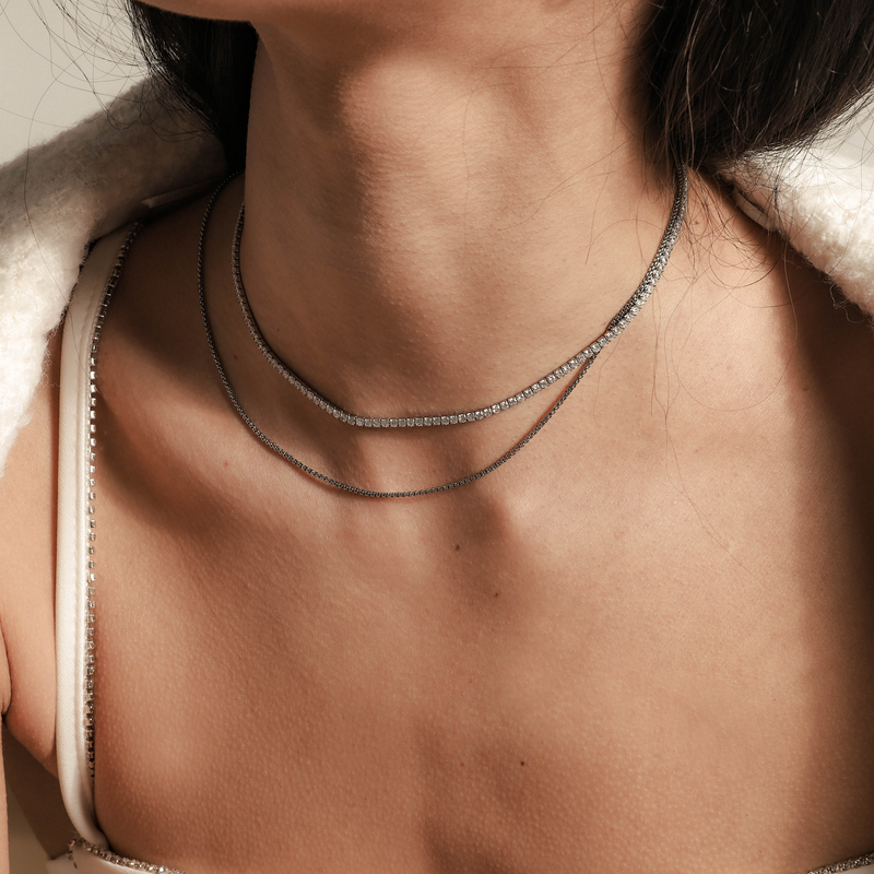Model wearing the TENNIS DAINTY NECKLACE SET which includes 14" and 16" necklaces.  One is Stainless steel Rhodium plated chain, 1mm Wide and the shorter one is a Rhodium-plated brass/cubic zirconia tennis necklace, 2 mm wide.