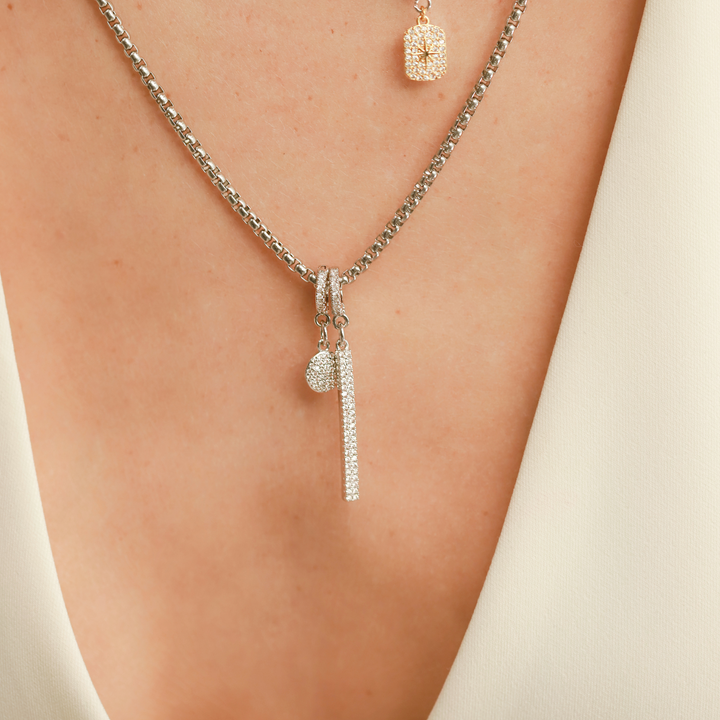 Model wearing a necklace in silver with two charms including the Dot Clip On Charm, a silver charm with a circular design fully encrusted with sparkling diamonds and a silver clip-on bale and the  bar charm. ||| SILVER