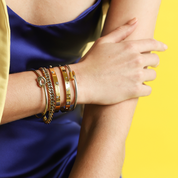 Model wearing the DYNAMIC STACK which is a 5 bangles stack, two 18k gold plated stainless steel bangles with Encrusted zirconia, the clavo wire bracelet in silver with gold nail details, knot bangle in silver and a chunky chain bracelet in mix gold and silver metals.