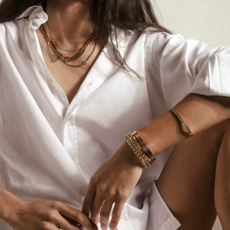 Model wearing the Maya Layered Necklace set and the BOLD STACK which is a 4 Pieces 18k gold plated stainless steel bangles set. It includes the Dynamic bracelet which has a bold knitting chain design, plain gold bangle, thin bangle with  Encrusted zirconia and another wider bracelet that has small bricks pattern on it.   