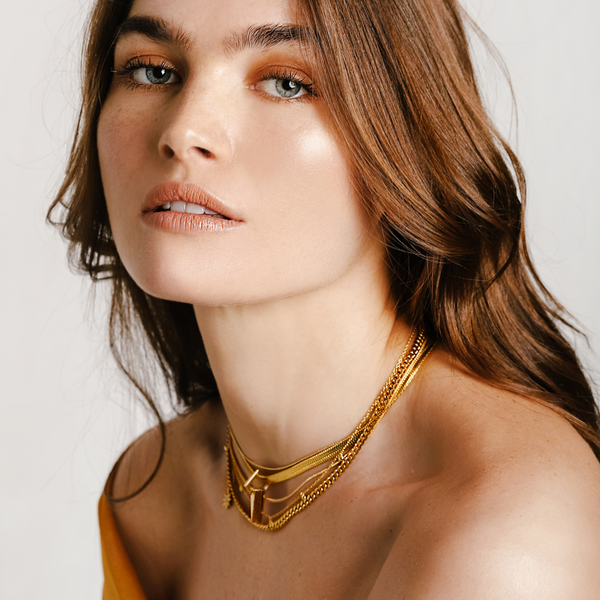 Model wearing the WILD LAYERED NECKLACE SET which includes 4 separate chains. One is a 16 inches Stainless steel 18k gold plated snake necklace with Triangle charms & Zirconia. 16inches Zirconia dot necklace. 17inches thin 18k gold plated necklace and an 18 inches gold chain necklace with tiny sunburst and zirconia stone charm.