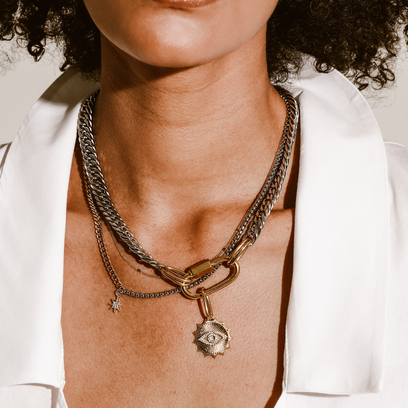 Model wearing the Maya Layered Necklace set which comes with three piece necklaces in stainless steel chunky chain with 18k gold plated carabiner and Zirconia evil eye pendant, plain silver thin chain  and another silver chain with starburst zirconia charm.
