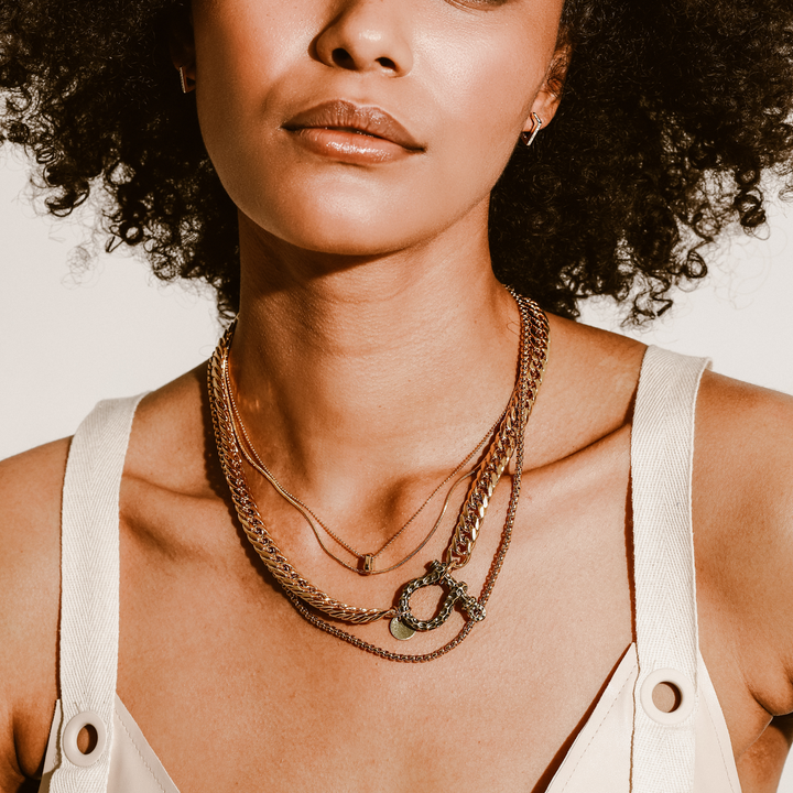 Model wearing the Le Giraffe Herradura necklace set which includes 3 separate chains, chunky gold chain with herradura clasp designed like giraffe skin with a small gold disc charm, short gold thin chain and long thin gold chain with circle charm.