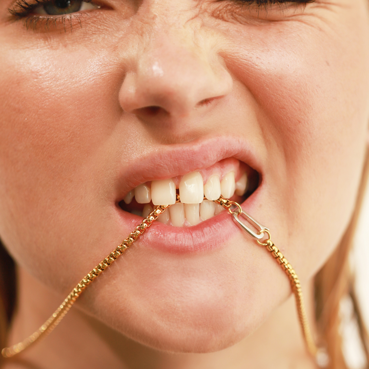 Model biting on the Classic Can Opener Box Chain Necklace featuring a distinctive gold link design and a silver can opener secure clasp.