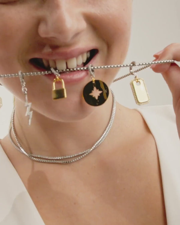 Video of a model wearing layered three necklaces with different charms. Charms included are the plaque,  compass, lightning bolt, north clip on charm and  The "Lock Clip on Charm" which is made of a Pave clip on Stainless steel 18k gold plated lock charm around 32mm in length.