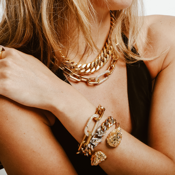 Model wearing a black halter top accessorized with the palma necklace and puerto Fino necklace both in gold and three bracelets. One is the Lion bracelet, Gold Tropicana bracelet and the Puerto Fino bracelet.