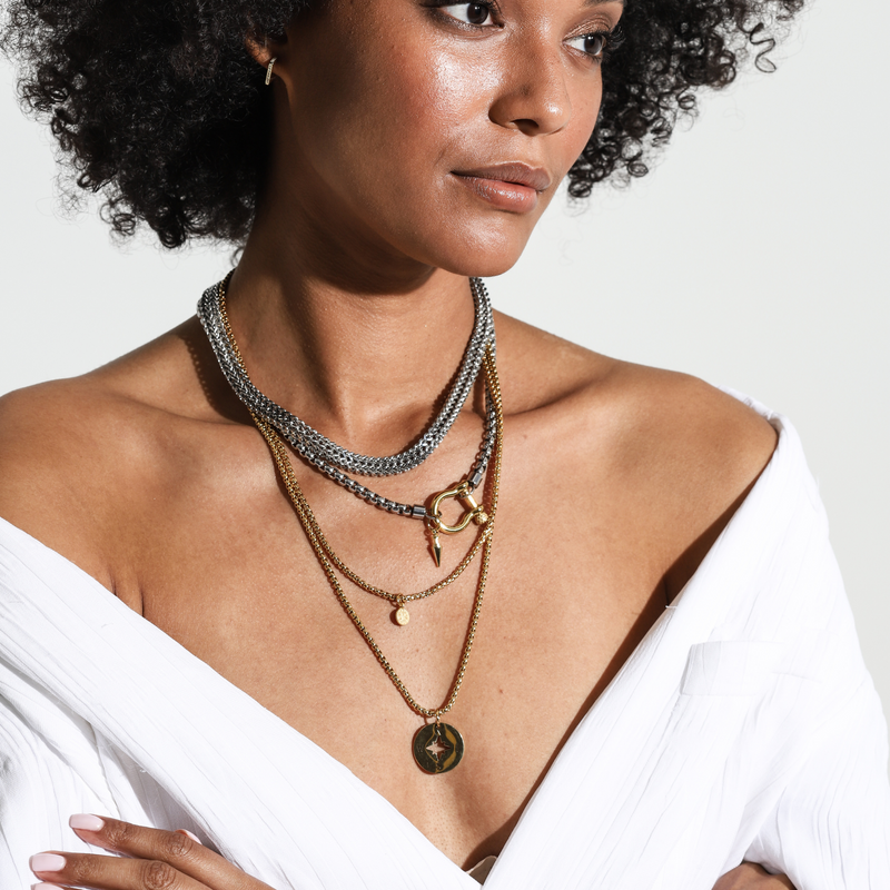 Model wearing the HERRADURA LAYERED NECKLACE SET in Gold variant which includes 4 separate chains. It includes the Marinero silver chain, Stainless steel chain with an 18k gold plated horseshoe clasp and spike pendant. The other necklaces are 2 thin gold plated chains with the compass disc and the ottoman disc pendants.