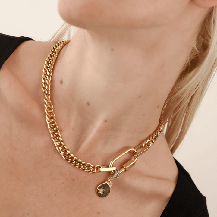 Model wearing a Gold-toned Cuban chain necklace with a carabiner clasp, featuring a star-shaped pendant and a diamond-encrusted rectangle pendant. Anne Clip On Star Necklace.