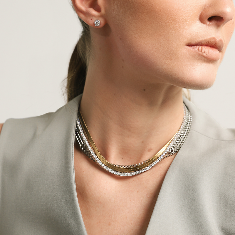 Model wearing the EXCITING NECKLACE SET which includes 3 layered necklaces, Stainless steel 18k gold plated snake necklace, Rhodium-plated brass/cubic zirconia tennis necklace and Stainless steel marinero silver chain. She is also wearing the BRIGHT SOLITAIRE EARRING.