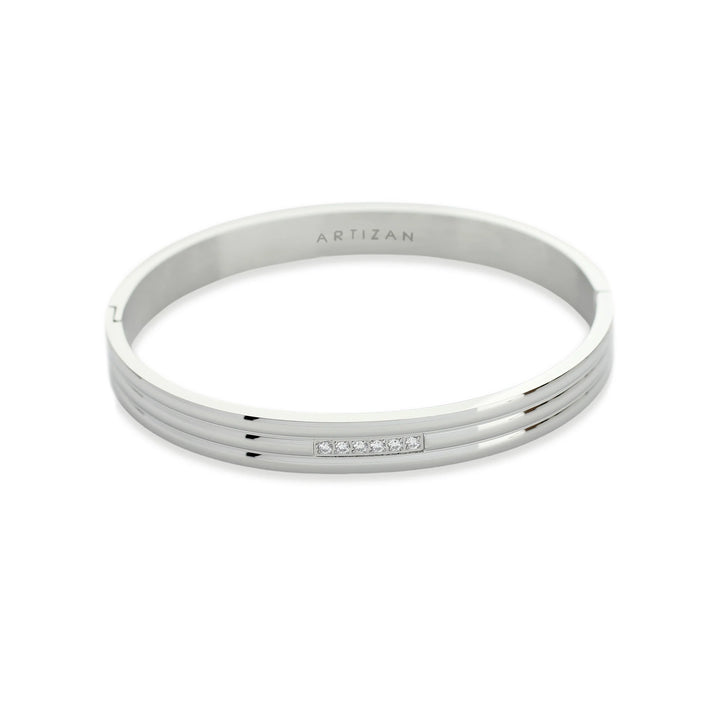 The Lane Bangle, which is a sleek silver bangle, features a minimalist design with a row of five sparkling stones set into its surface. The silver tone adds elegance and versatility, making it perfect for any occasion.