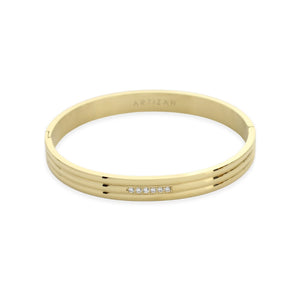 The Lane Bangle, a polished gold bangle featuring a sleek, minimalist design with a subtle row of sparkling stones on the front. This elegant bracelet can be worn solo or stacked with other bangles for a refined, sophisticated look, perfect for both casual and formal occasions.