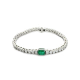 The Emerald Cut Tennis Bracelet, a silver bracelet with a classic tennis bracelet design, featuring an emerald-cut green gemstone centerpiece accented by shimmering diamonds.