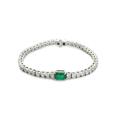 The Emerald Cut Tennis Bracelet, a silver bracelet with a classic tennis bracelet design, featuring an emerald-cut green gemstone centerpiece accented by shimmering diamonds.