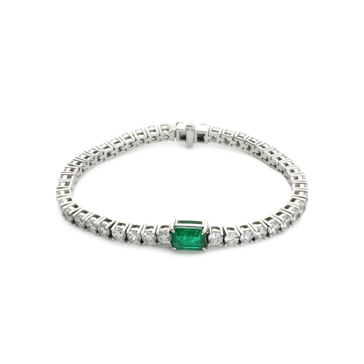 The Emerald Cut Tennis Bracelet, a silver bracelet with a classic tennis bracelet design, featuring an emerald-cut green gemstone centerpiece accented by shimmering diamonds.