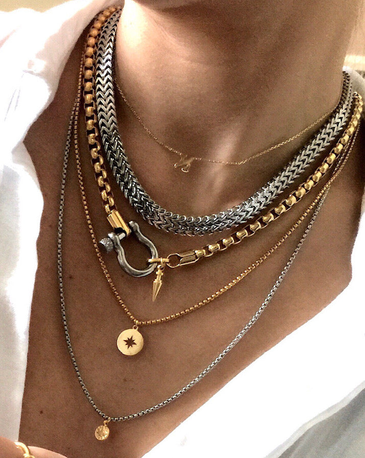 Model wearing the HERRADURA LAYERED NECKLACE SET in silver variant which includes 4 separate chains. It includes the Marinero silver chain, 18k gold plated stainless steel chain with an silver horseshoe clasp and gold plated spike pendant. The other two necklaces are the gold plated chain with the gold compass disc and silver chain with gold ottoman disc pendants.