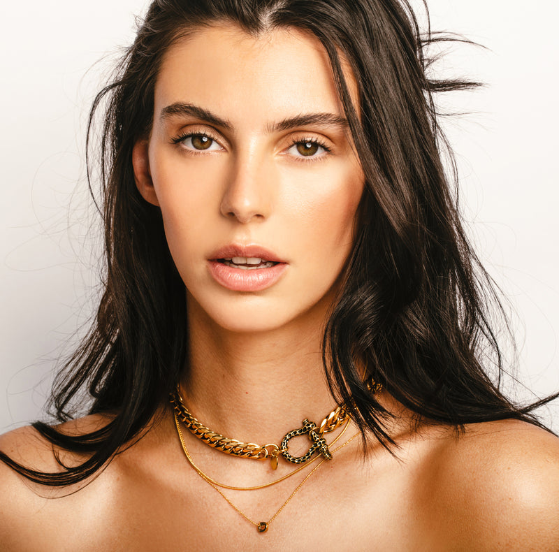 Model wearing the Le Giraffe Herradura necklace set which includes 3 separate chains, chunky gold chain with herradura clasp designed like giraffe skin with a small gold disc charm, short gold thin chain and long thin gold chain with circle charm.