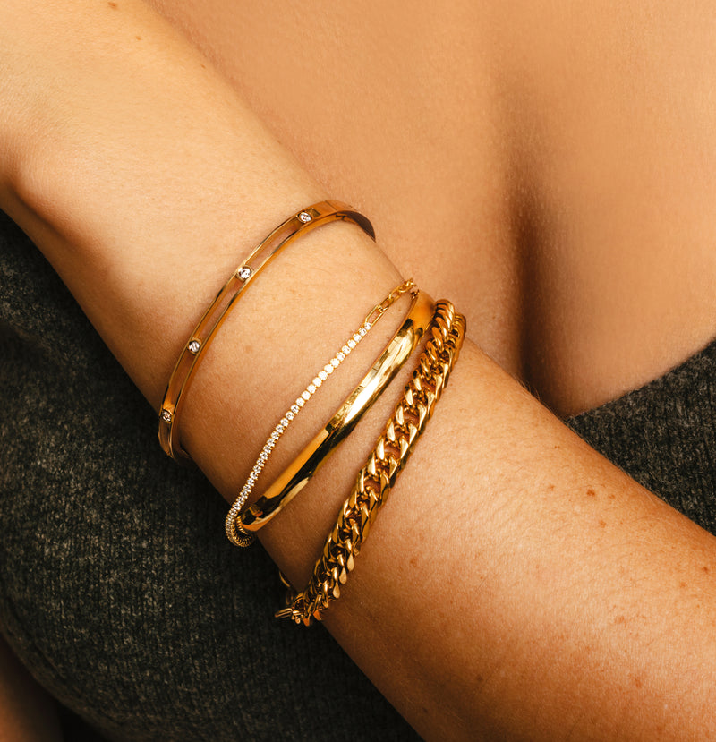 Model's left arm wearing the Chain Gold Stack comes with 4 gold bangles, one is a thin made of cubic zirconia bracelet, plain gold chain, Air bangle which is 4mm wide, gold plated with 8 zirconia dots in the middle and plain gold bangle.