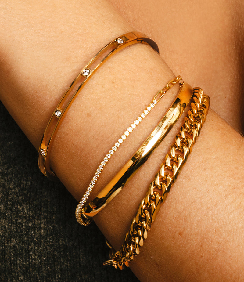 Women's wrist wearing 4 stacked bracelets,  gold tropicana chain , plain bangle, diamond studded and the air bangle which is gold with zirconia dots in the middle.