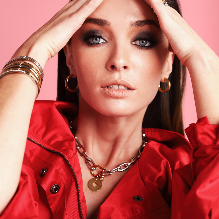 Model wearing gold hoop earrings stack of bangles and the HERRADURA PUERTO which is made of silver plated stainless steel chains with an 18k gold plated stainless steel horseshoe lock and a gold compass charm. 