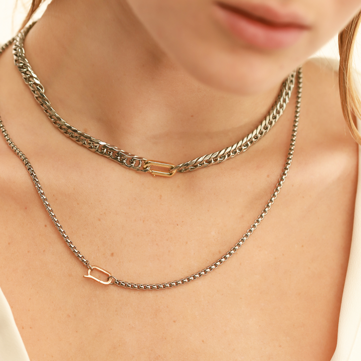 Model wearing two layered necklace. The Classic Can Opener Box Chain Necklace featuring a distinctive link silver chain design and a secure gold can opener clasp and the Can Opener Cuban necklace.