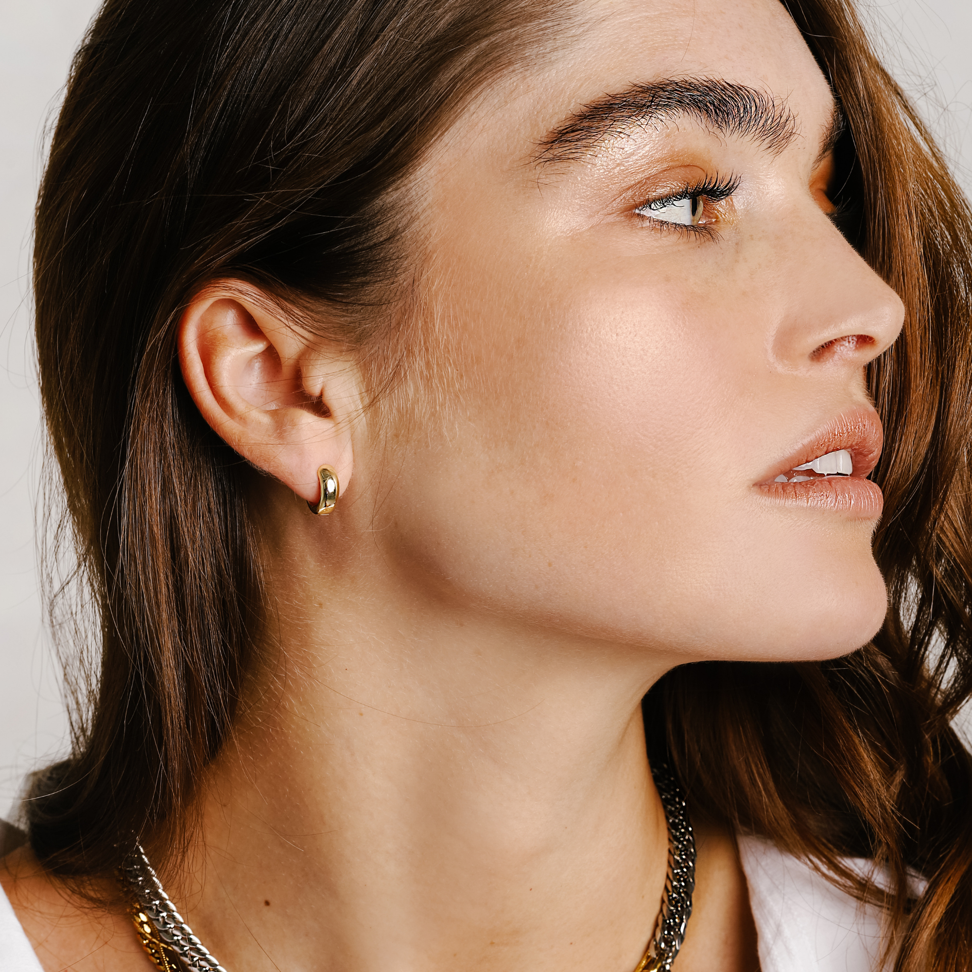 Model is wearing the VULCANO HUGGIES which is made of 18K gold plated 925 sterling silver with a 10mm outer diameter size. She is also wearing a silver necklace.