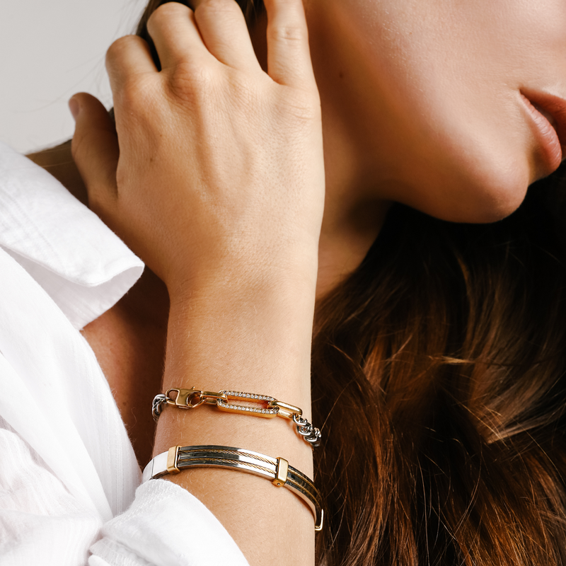 Model wearing the ISCHIA STACK which comes with a chain bracelet and a bangle. One is the Ischia bracelet which is a 7" Length Stainless steel chain with 18K gold plated lock and Zirconia charm and the Marinero bangle which is made of stainless steel with 18k gold plated details.