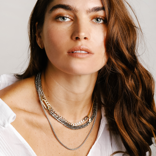 Model wearing the MADDALENA NECKLACE SET which includes 3 separate chains. One is a stainless steel chunky chain with gold oval link  with zirconia stones.  One is  a mix gold & silver chain with an 18k gold plated lightning charm and the longest is a plain stainless steel chain.