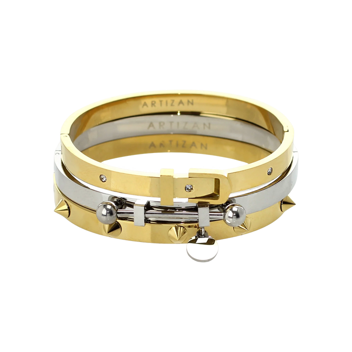 The BALANCE BRACELET STACK, a stylish three-piece bangle set featuring a mix of gold and silver tones with intricate details like a buckle clasp and studded accents. Perfect for adding a touch of edgy elegance to any outfit.