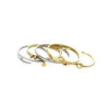 The Khanti Bracelet Stack, a five-piece gold and silver bracelet stack featuring bangles with a variety of  accents, including a knotted bangle, a buckle bangle with diamond-like stones, a bar bangle, and a bangle with diamond-like stones and a heart charm.
