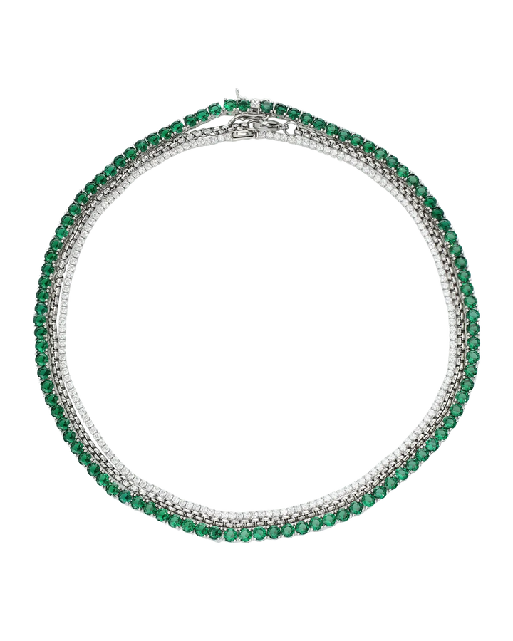 The Emerald Tennis Necklace Set, a three-piece silver necklace set featuring a single strand of emerald green gemstones, a single strand of white cubic zirconia, and a three-row necklace with alternating emerald green gemstones and white cubic zirconia.